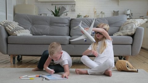 Brother draws picture with colored markers, sister plays with toy passenger airplane dreaming of becoming an airship pilot. Happy together brother and sister play together in room, sitting on floor