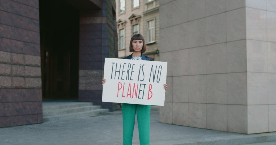 Young female holding there is no planet b phrase cardboard while standing at city street. Female student acrivist supporting eco campaign. Concept of environmental protection. Zoom in. Royalty-Free Stock Footage #1059513341
