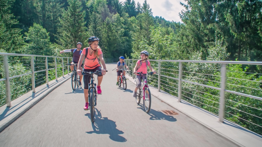 Slow motion of a family riding bikes among trees on an elevated path in Strekna, Slovenj Gradec