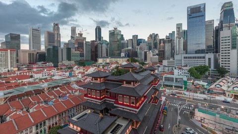The Buddha Tooth Relic Temple comes alive at night in Singapore Chinatown day to night transition timelapse, with the city skyline in the background. The temple is brightly lit with skyscrapers and