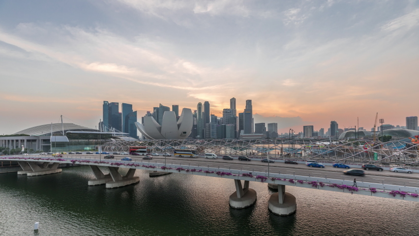 Aerial view over Helix Bridge and Bayfront Avenue with traffic day to night transition timelapse at Marina Bay from above with skyscrapers skyline on a background, Singapore