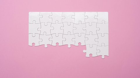 Top view of matching white rectangular jigsaw puzzle pieces on pink background, timelapse