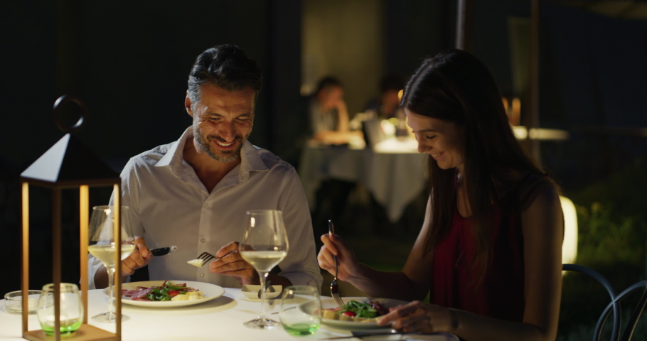 Happy elegantly dressed couple is enjoying romantic dinner together and cheering with white wine glasses to celebrate their anniversary and timeless love at well-served table at the luxury restaurant | Shutterstock HD Video #1059523355