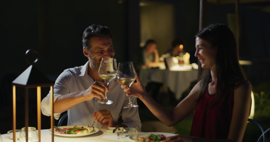 Happy elegantly dressed couple is enjoying romantic dinner together and cheering with white wine glasses to celebrate their anniversary and timeless love at well-served table at the luxury restaurant | Shutterstock HD Video #1059523355