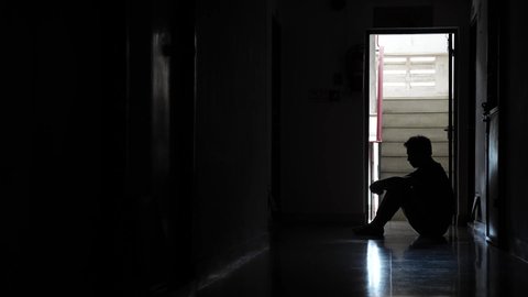 Silhouette of a sad man sitting in the dark leaning against the wall in old condo, Domestic violence, family problems, Stress, violence, The concept of depression and suicide