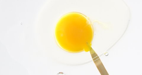 Popping and piercing egg yolk.Close-up Slow motion. Spilling egg yolk. white background.