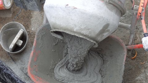 Concrete mixer pouring wet cement into wheelbarrow. A close up image of an electric concrete mixer pouring wet cement into wheelbarrow
