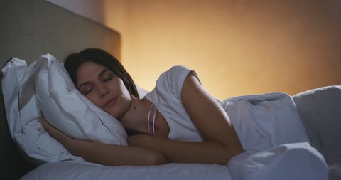 An young brunette woman is sleeping peacefully under warm duvet blanket in a cosy bed with switched on night lamp in a bedroom. Concept of comfort, relax,sleeping,health, bedding, softness,dreams