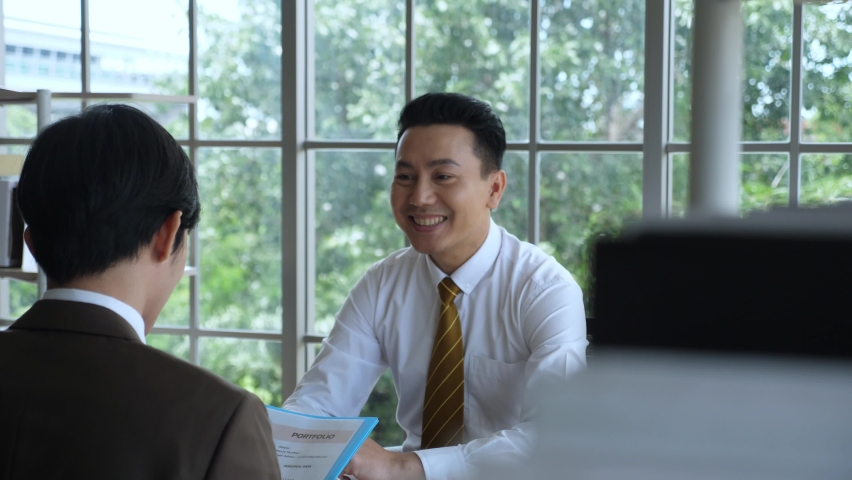 Business deal concept. Indoor, handheld, medium shot of Enthusiastic Asian businessman shaking hand, smiles, and talking to customer Royalty-Free Stock Footage #1059526208