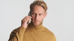 Young serious blond bearded man talking on smartphone over white background. No connection