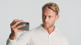 Handsome blond bearded businessman in shirt having video call on smartphone over white background