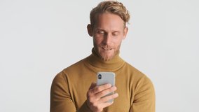 Young handsome blond bearded man emotionally using smartphone over white background