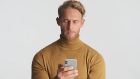 Young surprised blond bearded man using smartphone and smiling over white background