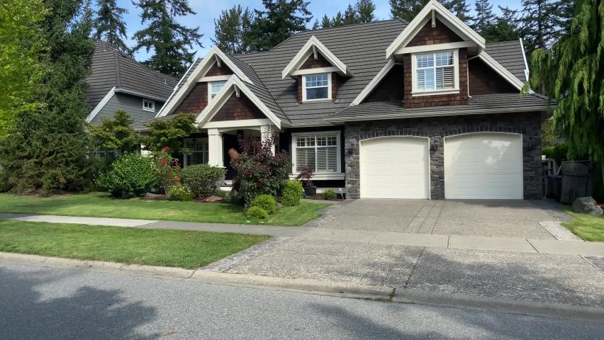 Establishing shot. Two story dark brown wood and stone luxury house with two garage doors, big trees and nice landscape in Vancouver, Canada, North America. Day time on September 2020. Tilt up. H.264. Royalty-Free Stock Footage #1059535202