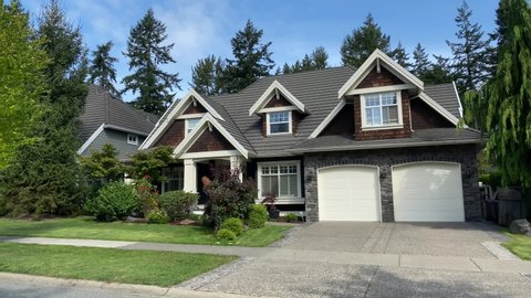 Establishing shot. Two story dark brown wood and stone luxury house with two garage doors, big trees and nice landscape in Vancouver, Canada, North America. Day time on September 2020. Tilt up. H.264.
