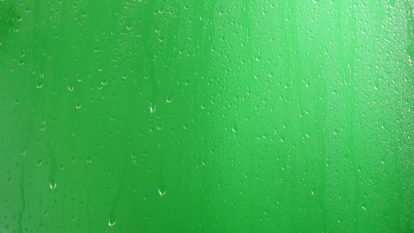 Water drops flow down the glass on a green background.