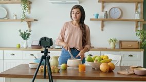 A Pretty Young Woman Shooting a Blog About Cooking. Video Blog of Healthy Food. Attractive Woman is Cooking on the Camera. Woman is Streaming Online Video Vlog.Girl Conduct Remote Teaching to Cooking