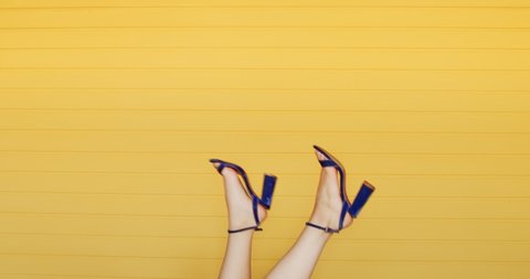 Feet of young woman in high-heeled footwear walking upside down in the air on yellow background. Fashionable womens shoes concept.