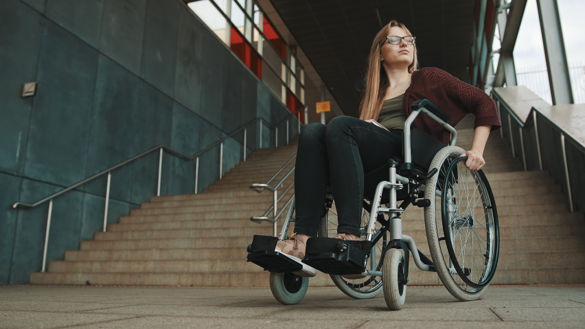 Young discouraged caucasian woman in the wheelchair in front of the staircase looking around for accessible way. High quality 4k footage | Shutterstock HD Video #1059544127