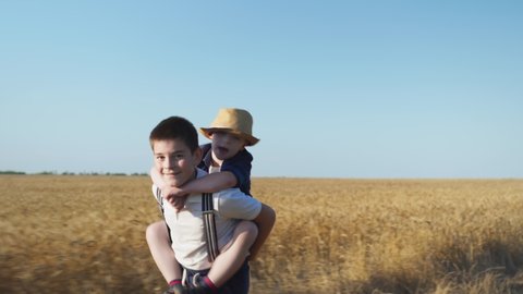 children have fun together in wheat field, boy carries a friend with down syndrome on his back