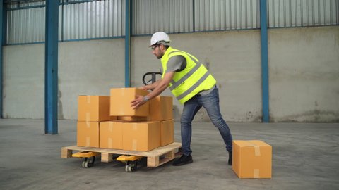 The engineer lifts the boxes to a cart and drags them in a warehouse.
