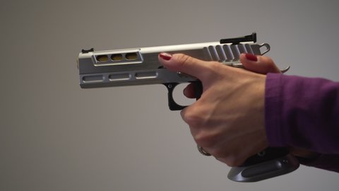 Close up of female with painted red nails, cocking and pulling trigger on large silver handgun