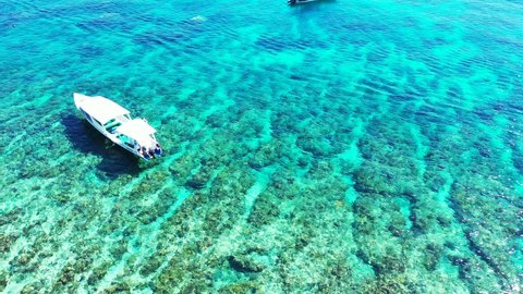 Island In Maldives - Boat Floating Over The Crystal Clear Sea Water With Coral Reef At The Bottom - A Beautiful Tourist Destination - Aerial Drone Shot