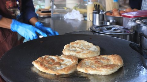 Street food vendor is preparing the dough and pan-frying paratha roti in hot oil until crispy on the outside.