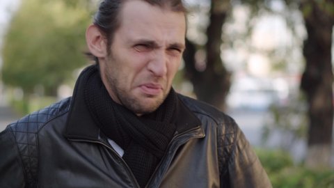 Young man in black jacket expressing disgust and disapproval with negative facial expressions outdoors.