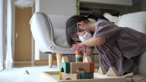 Asian 2 years girl in medical mask playing with wooden building blocks at home in the living room. Preschool toddler little child. Virus infectious disease measures Stock Video