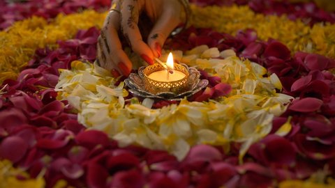 Closeup shot of an Indian female's hand decorating floral rangoli with a Diya. Hand of a woman lighting up a beautiful oil lamp placed in the center of a colorful rangoli - Diwali festival