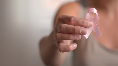 Woman hold pink ribbon. Close up view of hand with symbol of national breast canser awareness month in october.