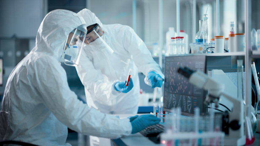 Medical Laboratory: Team of Microbiology Scientists Wearing Sterile Coveralls, Face Shields and Masks Talk, Use Computer to Analyse Blood Samples and Develop Vaccine, Drugs and Antibiotics.Danger Zone | Shutterstock HD Video #1059576371