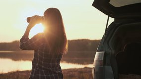 Finding strategy, Explore area, Find solution, Woman tourist. Woman looking through binoculars while standing by the water next to the car during dawn - Powered by Shutterstock - Get 15% off with code: PIKWIZARD15