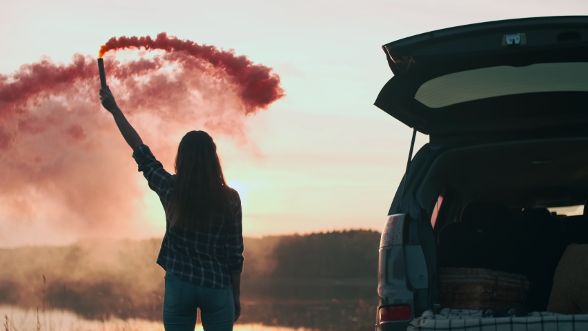 GO Everywhere.Signal fire, Colored smoke, Lost tourist, Happy woman. Woman tourist holds colored smoke in her hand and rejoices while standing near the car during sunset
