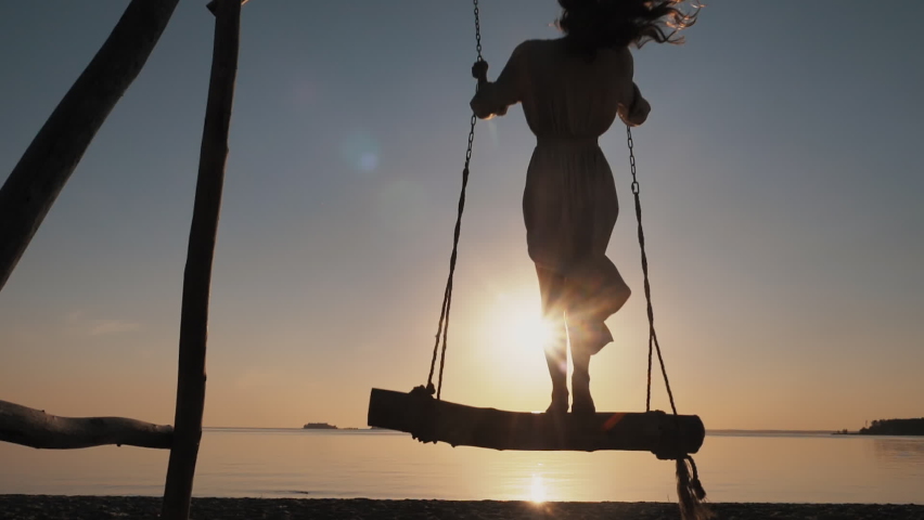 Silhouette of Young Carefree woman Swaying Standing on Wooden Swings on Amazing Evening Beach at Sunset Alone. Paradise Sea Relax, Summer Enjoyment, Serene Leisure, Free Happiness, Recreation Outdoors Royalty-Free Stock Footage #1059579380