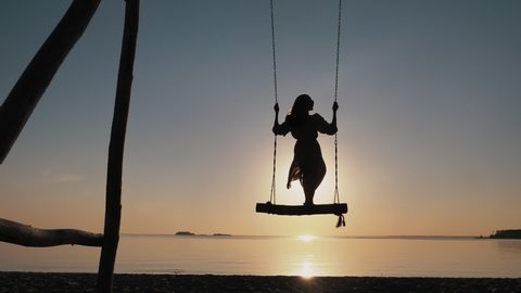Silhouette of Young Carefree woman Swaying Standing on Wooden Swings on Amazing Evening Beach at Sunset Alone. Paradise Sea Relax, Summer Enjoyment, Serene Leisure, Free Happiness, Recreation Outdoors