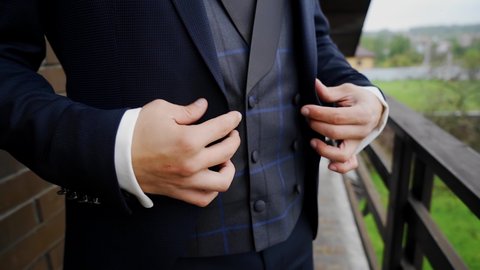 The guy is buttoning his jacket while standing on the balcony. Close-up of hands. : vidéo de stock