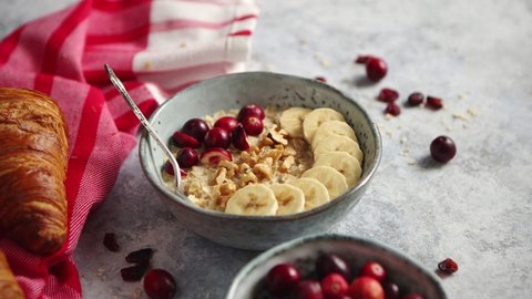 Ceramic bowl of oatmeal porridge with banana, fresh cranberries and walnuts on stone table top view in flat lay style. Healthy breakfast and diet food.