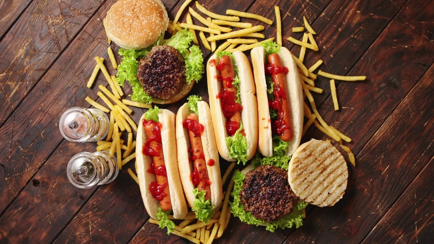 Hot dogs, hamburgers and french fries. Composition of fast food snacks. Placed on rusty wooden table. Top view. Royalty-Free Stock Footage #1059586118