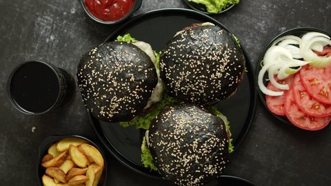 Top view of appetizing black hamburgers with sesame served on wooden board with crispy potato chips and ketchup and barbecue sauce