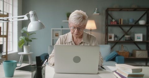 Pleased mature caucasian woman finishing her work. Remote senior worker closing her laptop and leaning on back of chair, joyfully smiling 4k footage
