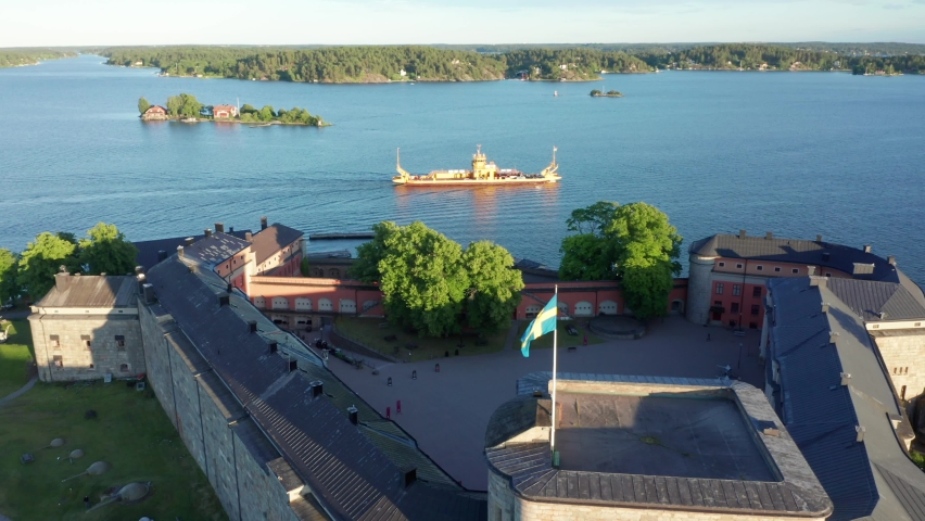 Sweden flag on castle outside Stockholm. Drone shot over palace and aerial view of Swedish archipelago and boats. Car transportation inter island connection vessel in Vaxholm 