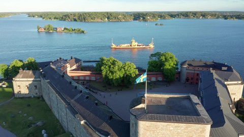 Sweden flag on castle outside Stockholm. Drone shot over palace and aerial view of Swedish archipelago and boats. Car transportation inter island connection vessel in Vaxholm 