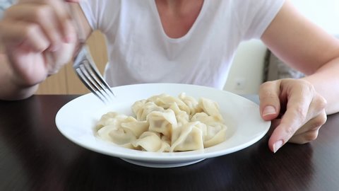 A hungry woman eating dumplings in the kitchen at home, convenience and rapid cooking food concept, close up view of a ceramic plate full of ravioli.