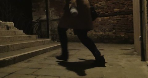 Steadicam shot of a woman with phone running at night. She escaping from maniac in dark narrow passage between old worn buildings