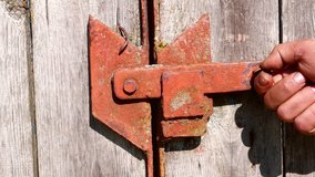 Open and close the iron bar of the wooden gate by hand. Metal rusty bolt of wooden doors. Open the door. Lock the door. Active action of the human hand. Video. - Powered by Shutterstock - Get 15% off with code: PIKWIZARD15