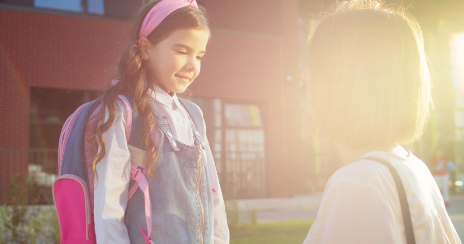 Close up portrait of Caucasian beautiful woman fixing clothes on cute little daughter outdoor in sun lights. Side view of happy mother send girl pupil to school on sunny morning Back to school concept