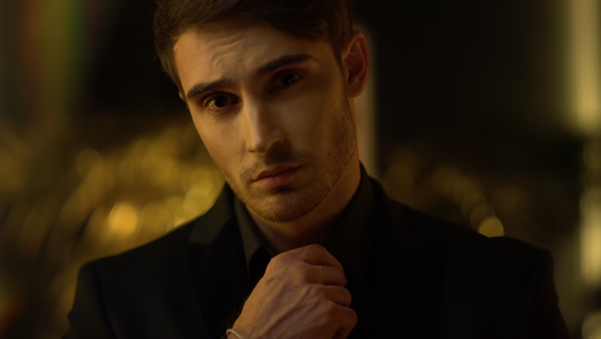Portrait of young business man posing at dark office. Closeup gorgeous man face smiling at camera indoors. Rich charming businessman touching shirt collar inside at night.