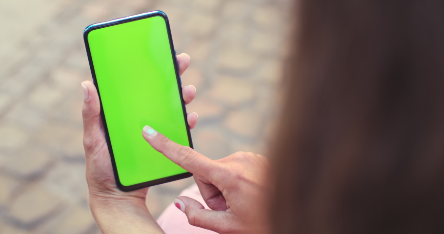 Over shoulder view of female person holding and pressing on smartphone with mockup screen while sitting at street. Concept of chroma key and greenscreen | Shutterstock HD Video #1059623042